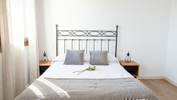 A neatly made bed with a patterned bedspread, two pillows, and a single flower. There are two bedside tables with lamps. - Pico Rubia, two bedroom apartment, living room, kitchen and bathroom (Ampuero)