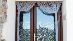 A wooden door with a glass panel, flanked by curtains, and a stone wall to the left. - Pico Rubia, two bedroom apartment, living room, kitchen and bathroom (Ampuero)