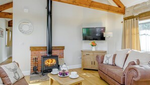 Ein gemütliches Wohnzimmer mit Kamin aus Ziegelsteinen, Holzbalken, Fernseher und einer Couch.