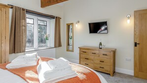 Ein Schlafzimmer mit einem großen Bett, einer Holzkommode, einem Fernseher und einem Fenster mit Vorhängen.