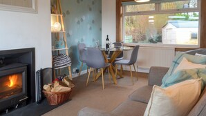 A cozy living room with a fireplace, a dining area with a table and chairs, and a large window with a view of the outside. - 2 bedroom accommodation in Ellenabeich, near Oban (Ellenabeich, near Oban)