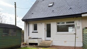 A single-story house with a sloped roof, a front door, and a small porch. - 2 bedroom accommodation in Ellenabeich, near Oban (Ellenabeich, near Oban)