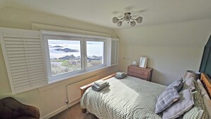 A bedroom with a bed, a dresser, a chair, a ceiling fan, and a window with a view of the sea. - 2 bedroom accommodation in Ellenabeich, near Oban (Ellenabeich, near Oban)