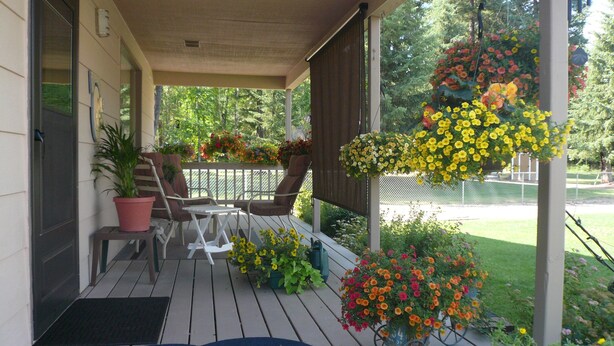 A covered porch with a table and chairs, surrounded by potted plants and hanging flower baskets. - GUEST CABIN IN THE WOODS (Bigfork)