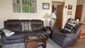A living room with a brown leather sofa, a matching armchair, a small wooden coffee table, and a floor lamp. - GUEST CABIN IN THE WOODS (Bigfork)
