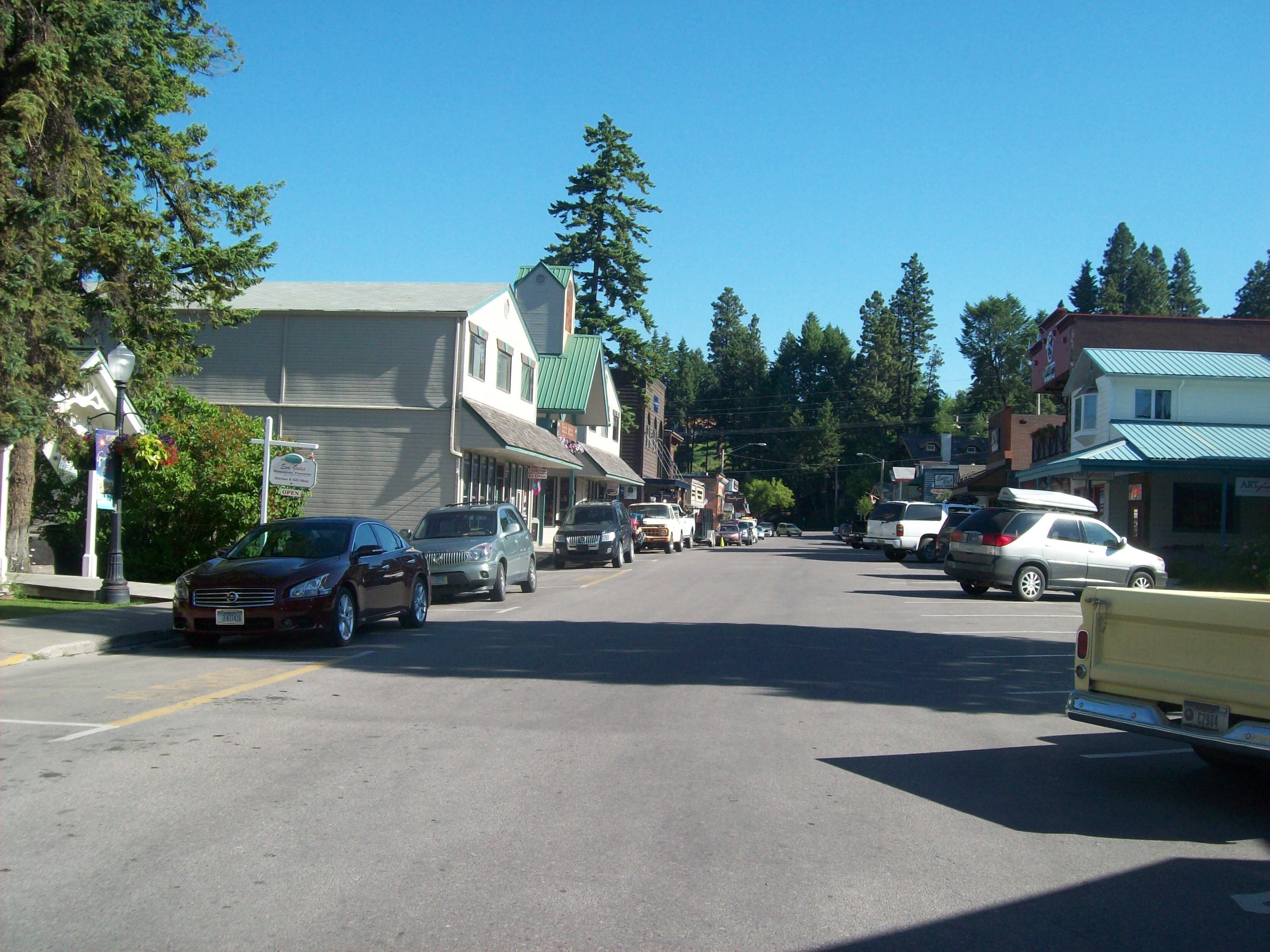 A street view with parked cars, buildings, and trees.