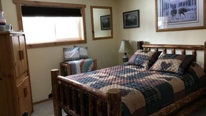 A bedroom with a wooden bed, a dresser, a window with blinds, and framed pictures on the wall. - GUEST CABIN IN THE WOODS (Bigfork)