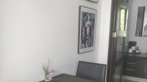 Een eethoek met een tafel en stoelen, een kunstwerk in een lijst aan de muur, en een koffieapparaat op de achtergrond.