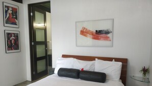 Hotelkamer met een bed, nachtkastje, een lijst met abstract schilderij en een deur naar een andere kamer.