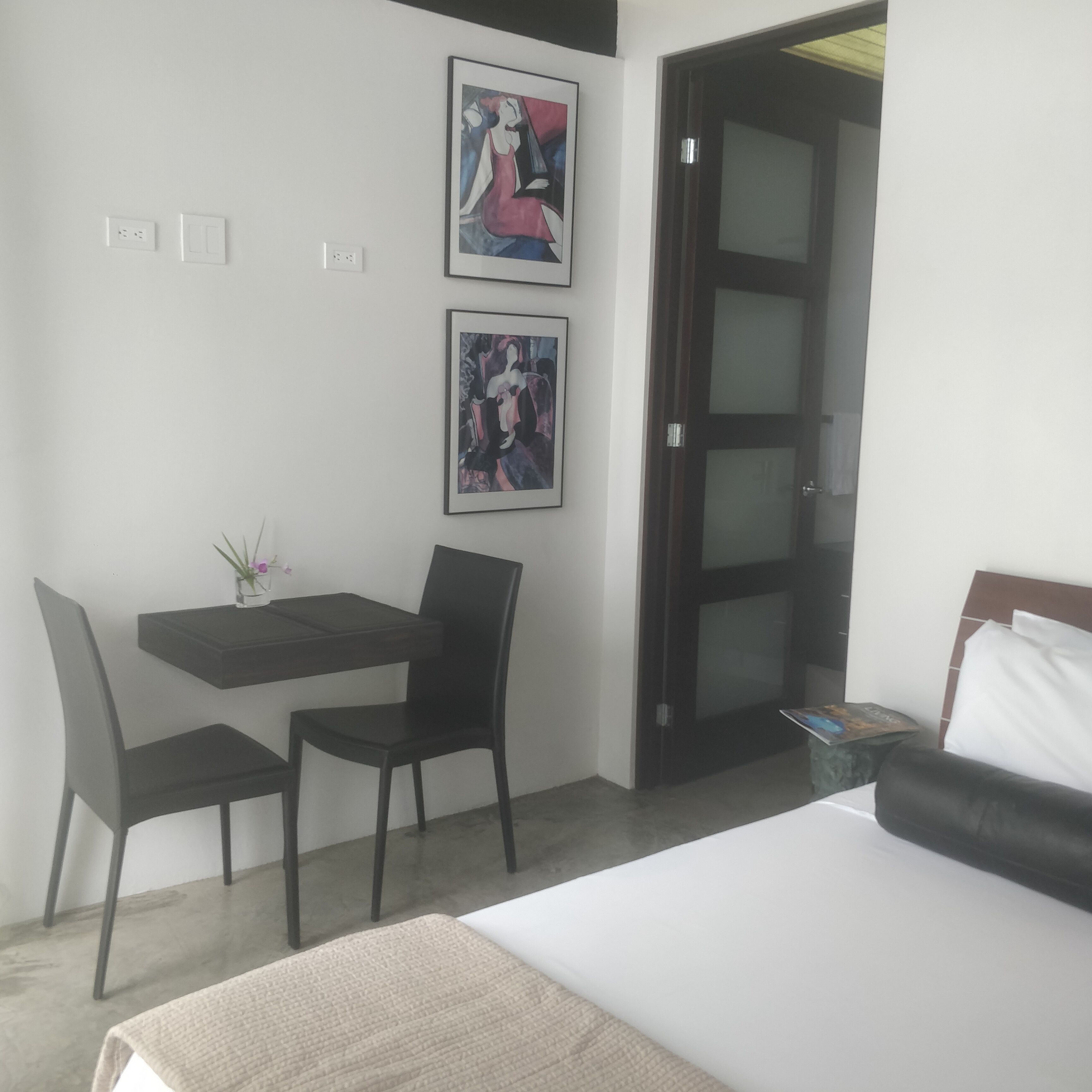 Een hotelkamer met een bed, een bureau met twee stoelen en twee ingelijste kunstwerken aan de muur.
