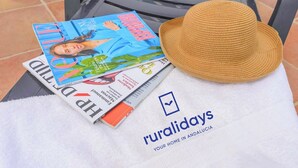 Uma revista, um chapéu de palha e uma toalha com o logotipo 'ruralidays' em uma cadeira.