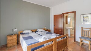 Quarto com duas camas, uma mesa de cabeceira de madeira, uma escrivaninha, uma cadeira e banheiro com pia e espelho.
