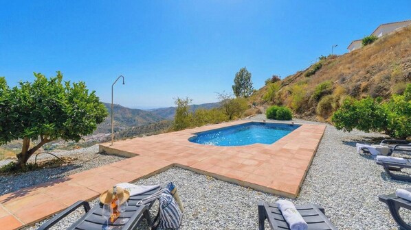 A rectangular pool with a tiled deck, surrounded by gravel and small trees.