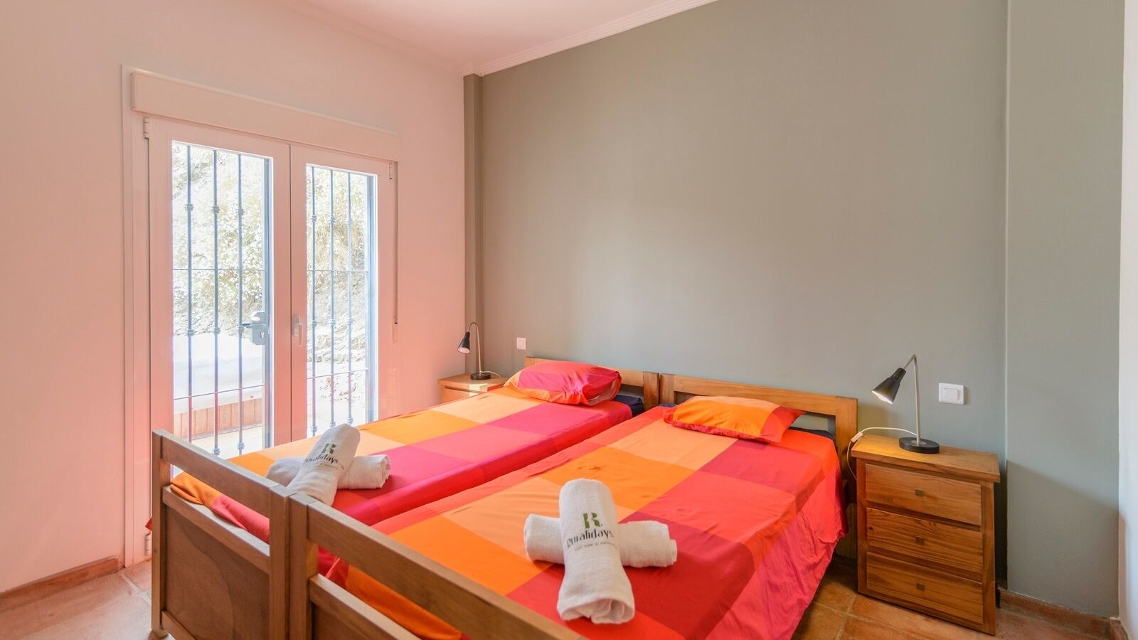 A double room with two beds, each with a wooden headboard, and a small wooden nightstand with a lamp.