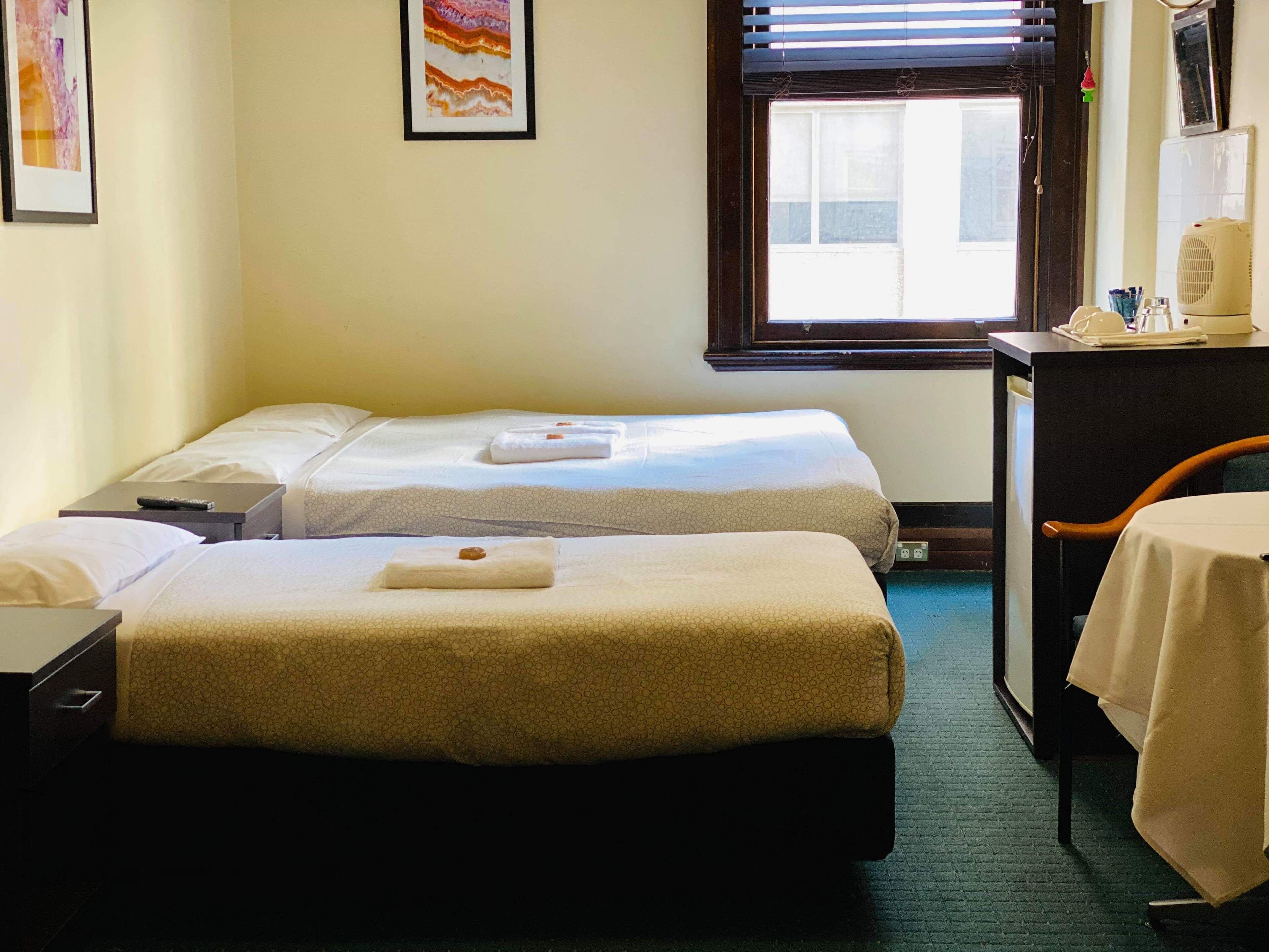 Een hotelkamer met twee bedden, een bureau, een stoel en een raam met zonwering.