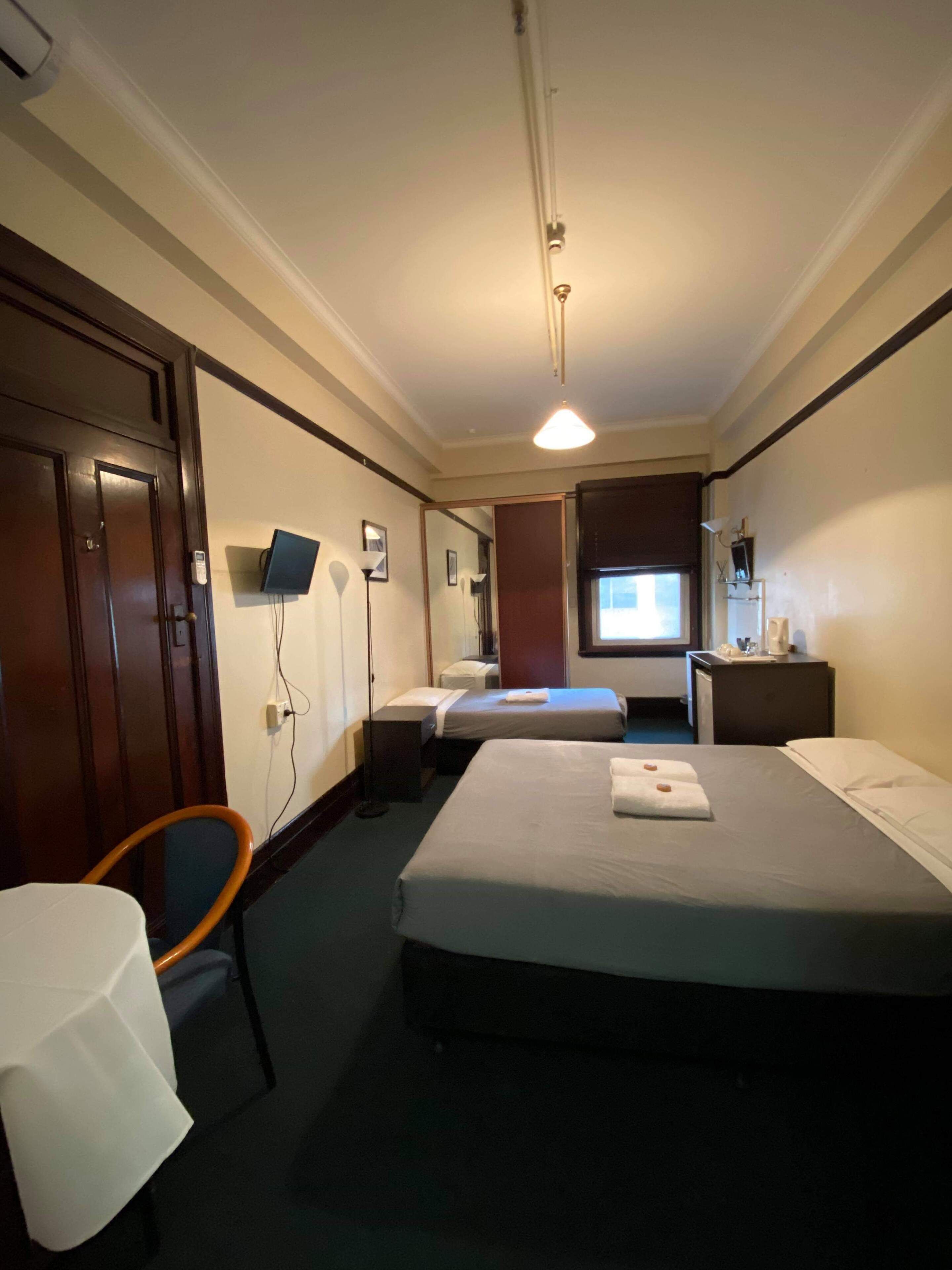 Quarto de hotel com duas camas, uma escrivaninha, uma cadeira, uma televisão e um espelho.