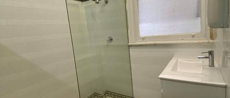 Un baño con cabina de ducha de vidrio, un lavabo con espejo y un inodoro.