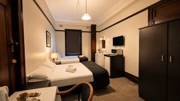 A hotel room with two beds, a desk with a microwave, a TV, and a wardrobe.