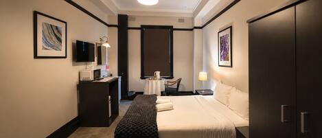 Habitación de hotel con cama, mesita de noche, lámpara, televisor y obras de arte en las paredes.