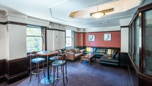 A spacious lounge area with a round table, bar stools, sofas, and a patterned carpet. - The Occidental Hotel (Sydney)