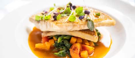 A plate of food with a fish fillet, vegetables, and a sauce.