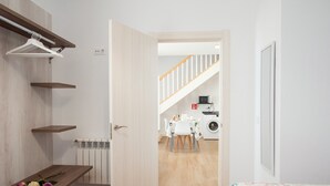 A bedroom with a bed, a wooden shelf with flowers, a door leading to a kitchen with a washing machine. - Pico Negro- apartment with two bedrooms, living room, kitchen and bathroom (Ampuero)