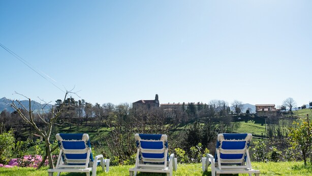 Three white lounge chairs with blue cushions facing a scenic view of a hill with buildings and trees. - Pico Negro- apartment with two bedrooms, living room, kitchen and bathroom (Ampuero)