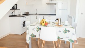 A compact kitchen with a washing machine, a microwave, and a refrigerator. There is a dining table with a cactus-patterned tablecloth and chairs. - Pico Negro- apartment with two bedrooms, living room, kitchen and bathroom (Ampuero)