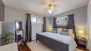 Une chambre à coucher avec un lit, un ventilateur de plafond, une télévision et une fenêtre avec des rideaux.