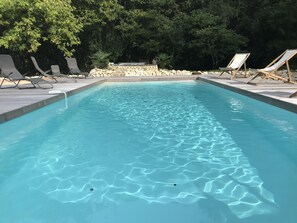 A rectangular swimming pool with clear blue water, surrounded by a stone wall and wooden deck. - traditional Landes house 16 people spa, swimming pool, billiards (Cachen)