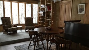 A cozy living room with a wooden floor, a round wooden table, and several chairs. There is a bookshelf with various items and a television on a stand. - Northwoods Best @  Amazing Grace Retreat Fantastic fishing, Awesome Relaxation! (Sayner)