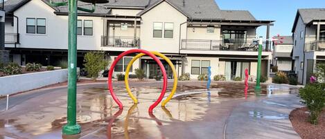 A residential area with modern houses, a wet pavement, and colorful playground equipment.