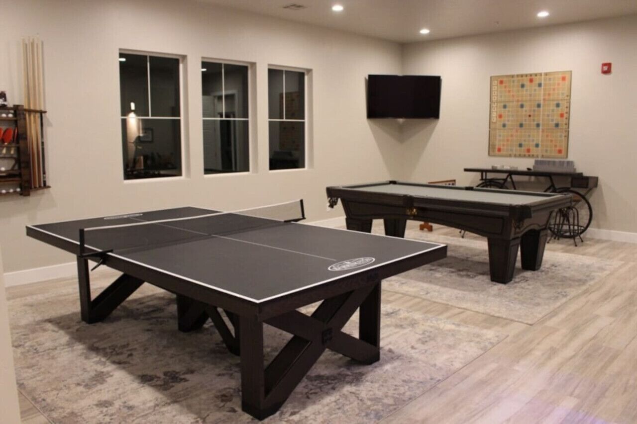 A room with a ping pong table, a pool table, and a television on the wall.