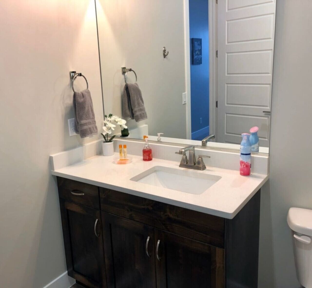 A bathroom with a white sink, dark wooden cabinets, a mirror, and a toilet.