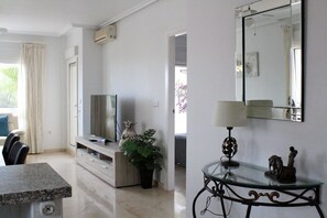 Una sala de estar moderna con televisor de pantalla plana, comedor con encimera de granito y una lámpara decorativa.