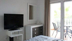 A hotel room with a bed, a TV on a stand, a dresser, and a balcony with chairs. - 2 Bed 2 Bath South Facing Apt, Quiet But Near Beaches and Amenities (Orihuela)