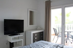 Habitación de hotel con cama, televisor en un soporte, cómoda y balcón con sillas.