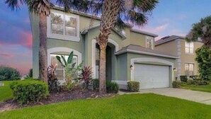A two-story house with a garage, surrounded by well-maintained lawns and tropical plants. - Gathering Resort Pool/Spa Home-Mins away to the PARKS (Kissimmee)