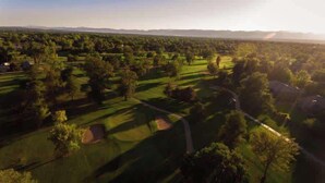 Une vue aérienne d’un parcours de golf avec plusieurs trous, des arbres et un ciel dégagé.