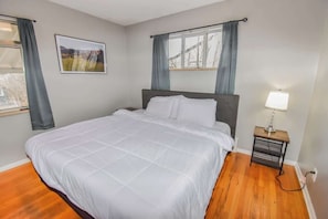 A bedroom with a bed, a nightstand with a lamp, a window with curtains, and a framed picture on the wall. - Family Home with Large Yard & Golf Theme Near Rail (Denver)