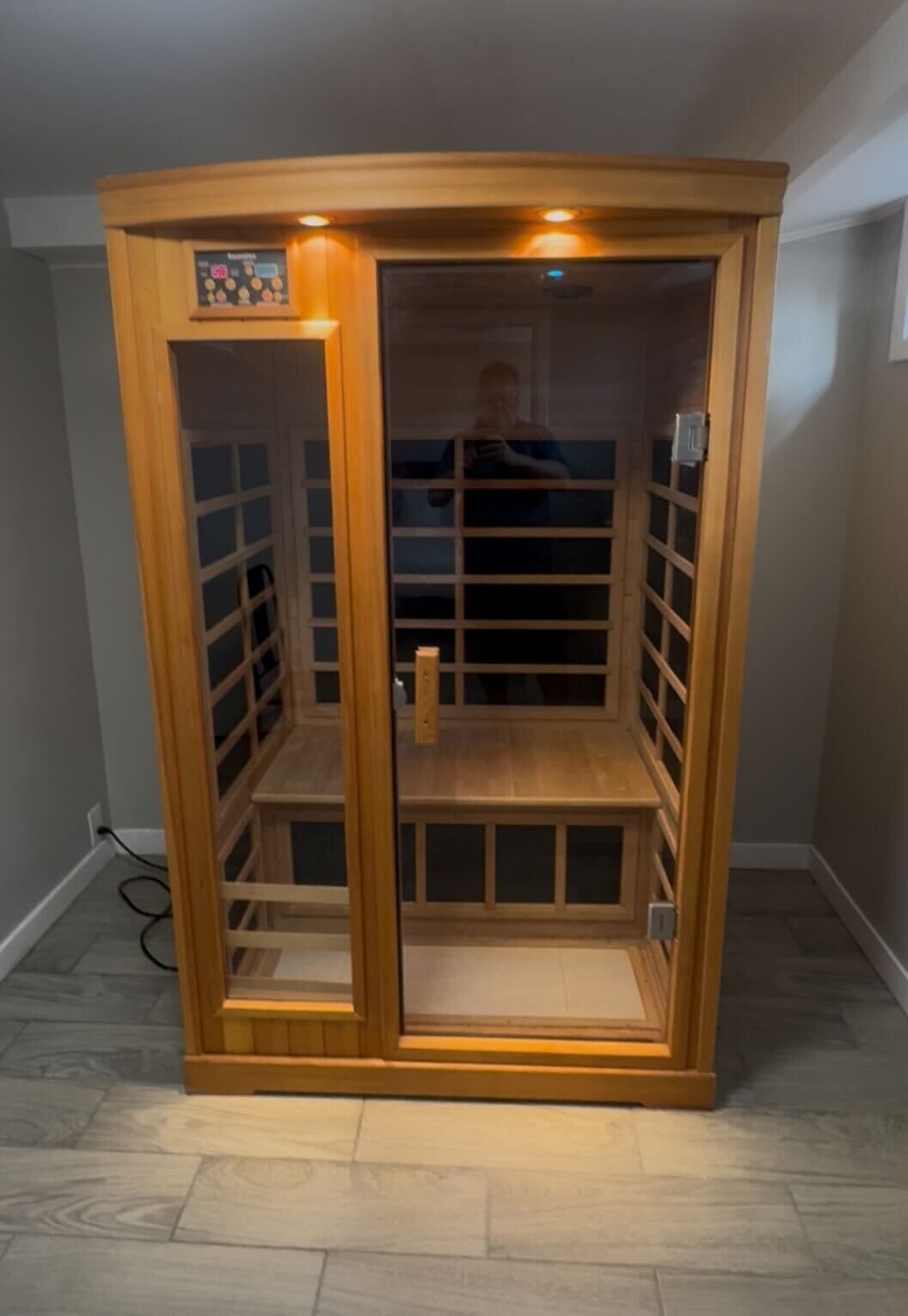A wooden sauna with a glass door, a control panel, and a small shelf.