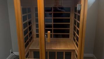 A wooden sauna with a glass door, a control panel, and a small shelf.