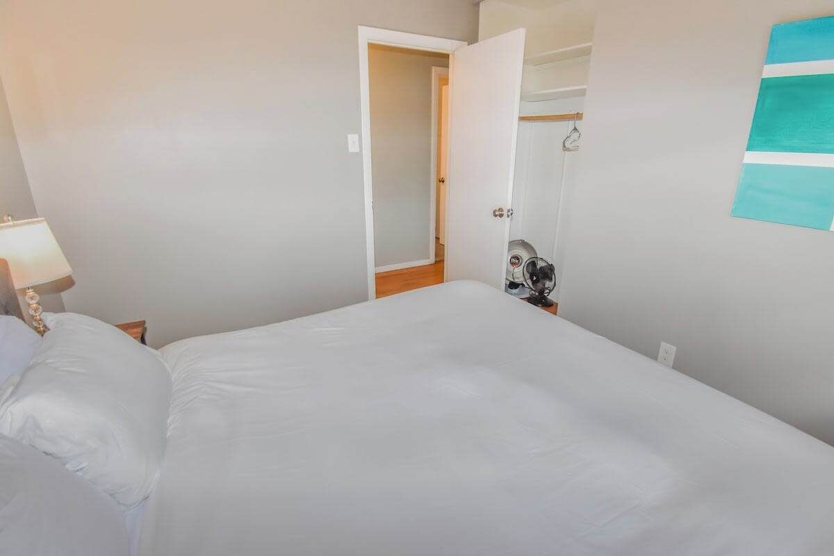 Une chambre avec un grand lit, une table de chevet avec une lampe, une porte donnant sur une autre pièce et un porte-serviettes fixé au mur.