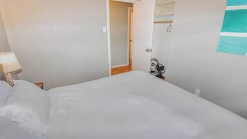 Une chambre avec un grand lit, une table de chevet avec une lampe, une porte donnant sur une autre pièce et un porte-serviettes fixé au mur.