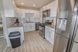 A modern kitchen with white cabinets, stainless steel appliances, and a black trash bin. - Family Home with Large Yard & Golf Theme Near Rail (Denver)