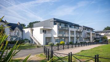 Un immeuble résidentiel moderne à plusieurs étages, doté d’un toit plat, de grandes fenêtres et d’une entrée sécurisée par un portail.