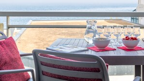 Ein Tisch mit einer Karaffe, Gläsern, Schüsseln und einem roten Kissen auf einem Balkon mit Meerblick.