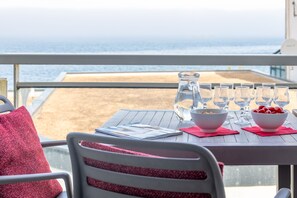 A table set with a pitcher, glasses, bowls, and a red cushion on a balcony overlooking the sea. - Abordable Près de la Plage | Accès Piscine (Plougasnou)