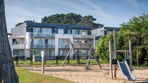 Ein Spielplatz mit Rutsche und Schaukeln, umzäunt, mit einem Gebäude im Hintergrund.