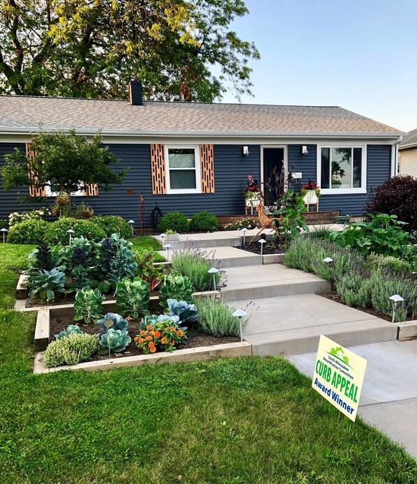 Une maison d’habitation dotée d’un jardin bien entretenu, d’une plaque indiquant qu’elle a reçu un prix pour son esthétique extérieure et d’un numéro de maison bien visible.